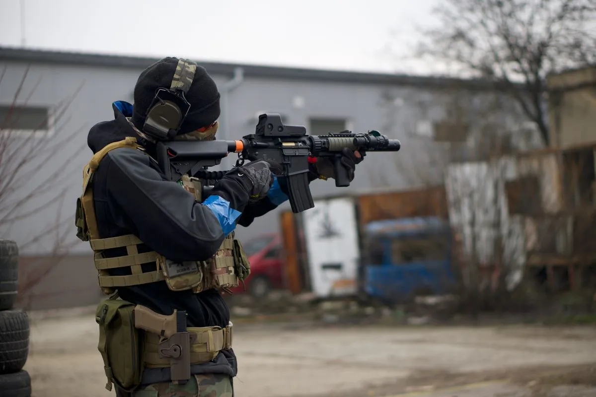 An airsoft player in tactical gear aiming beside an old building