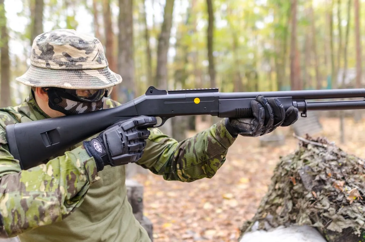 An airsoft player in a bush hat aiming a pump action replica in a forest
