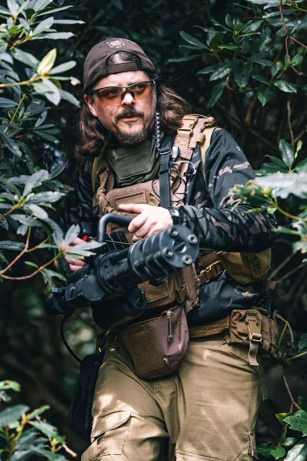An airsoft player with a replica minigun among rhododendron bushes