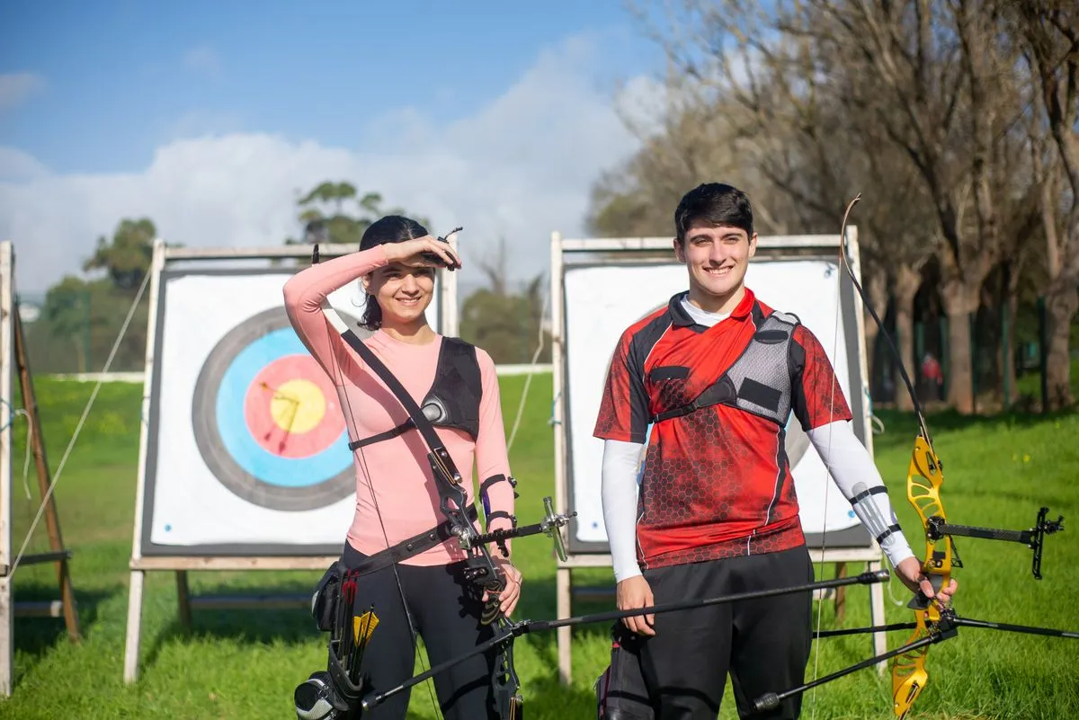 Two archers smiling in front of colourful targets on a sunny range