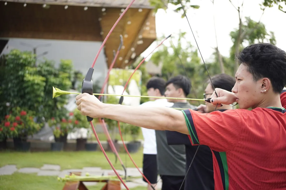 A group of young adults shooting bows on a lawn