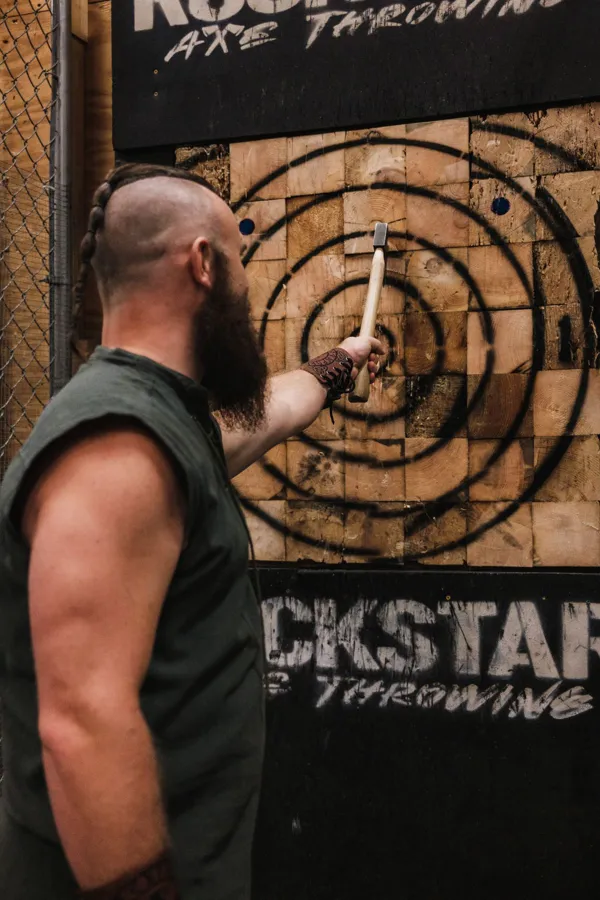 Adult man engaging in axe throwing indoors for fun and recreation.