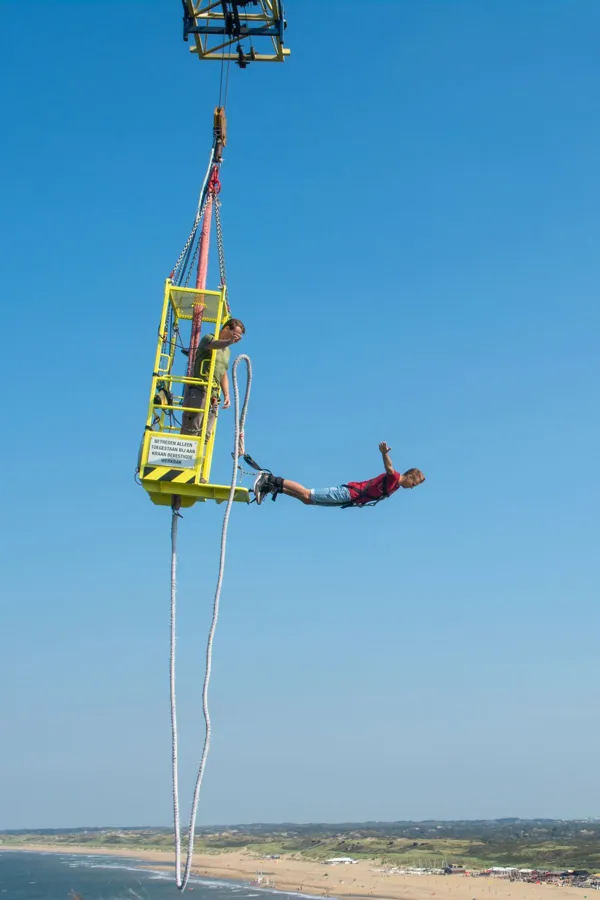 A bungee jumper hanging from a crane cage above a beach under a blue sky