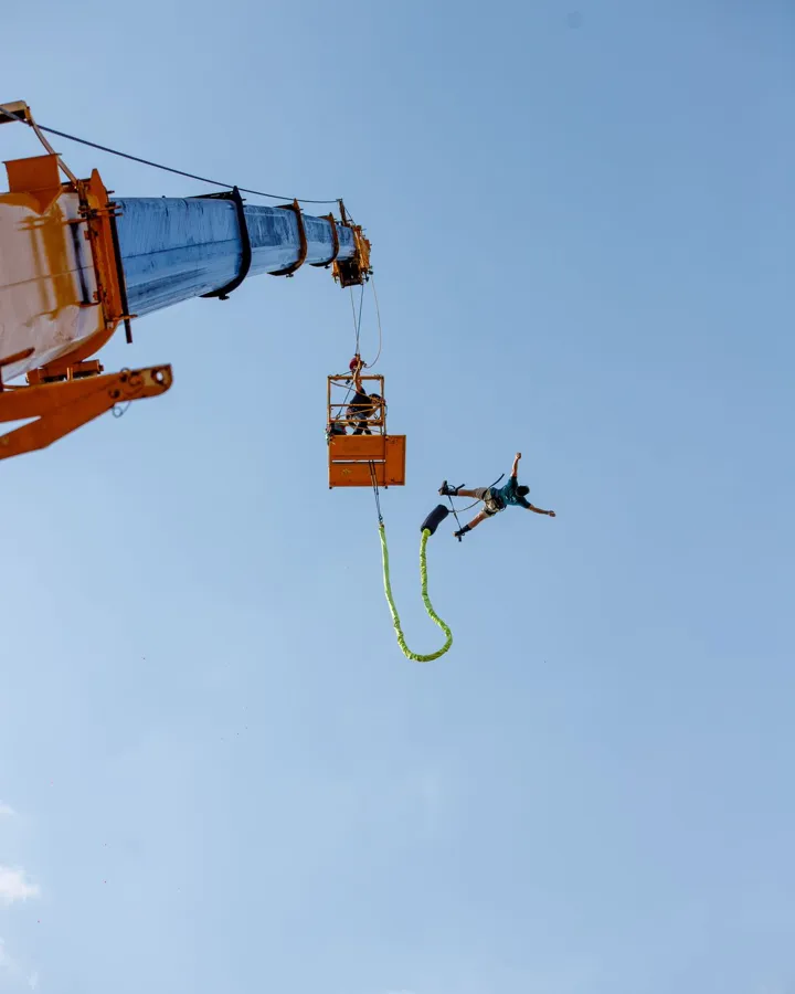 A bungee jumper falling from a crane platform against a clear blue sky