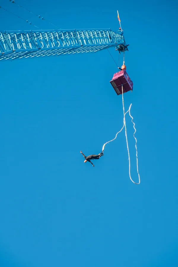 A crane cage and a bungee jumper high up against a bright blue sky