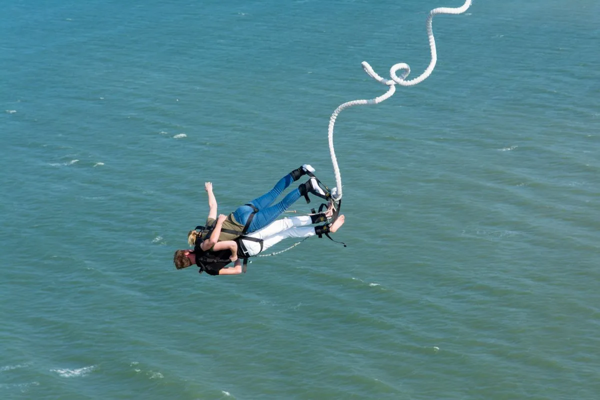 A bungee jumper in mid fall above green water