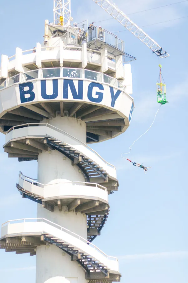 A tall spiral tower with the word Bungy on it and a jumper falling beside it