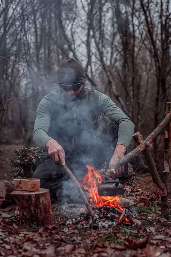 A person cooking over a campfire in woodland