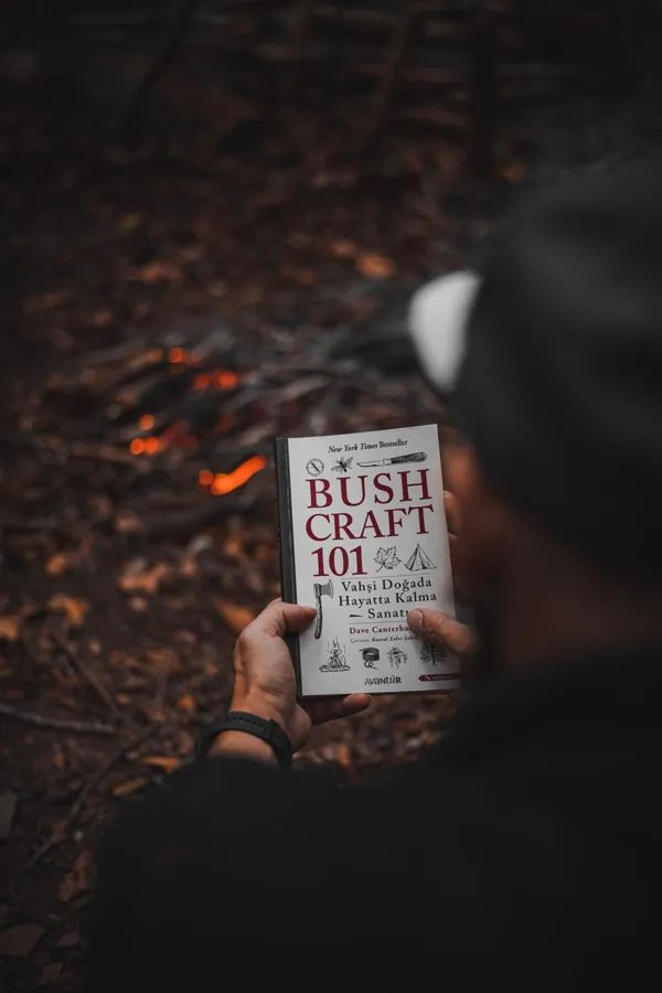 A person with a bushcraft book beside a campfire