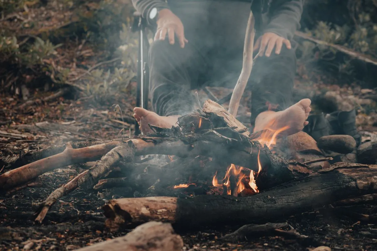 A man seated by a campfire outdoors in the woods.