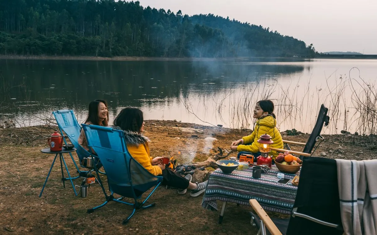A camping scene by a lake at sunset with friends