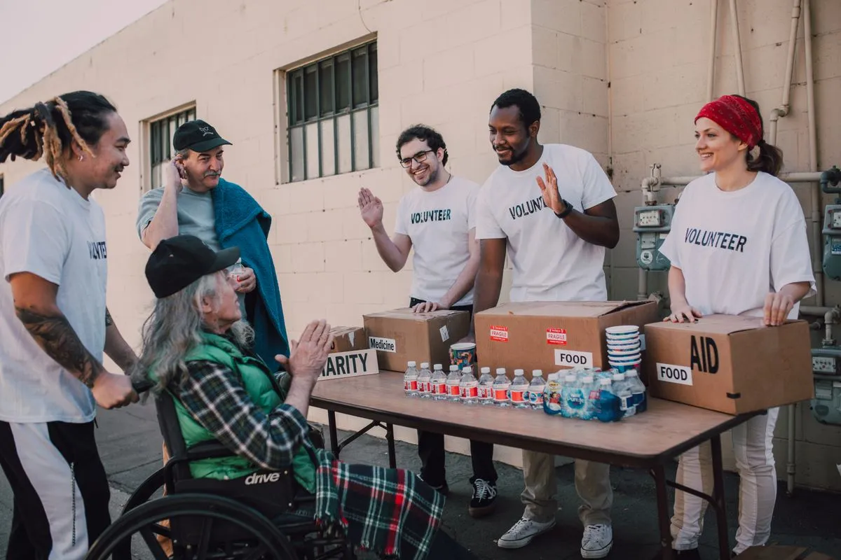 Volunteers handing out food and aid to a person in a wheelchair outdoors.