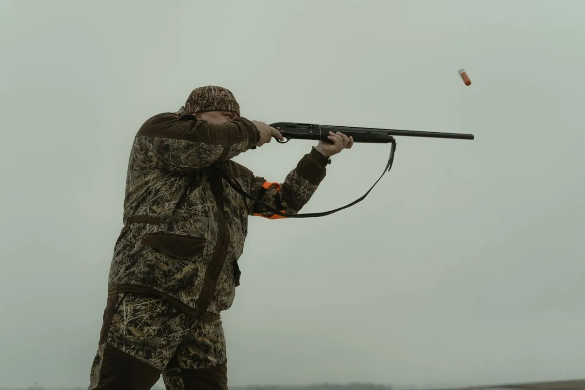 A shooter firing a shotgun with a spent cartridge flying out