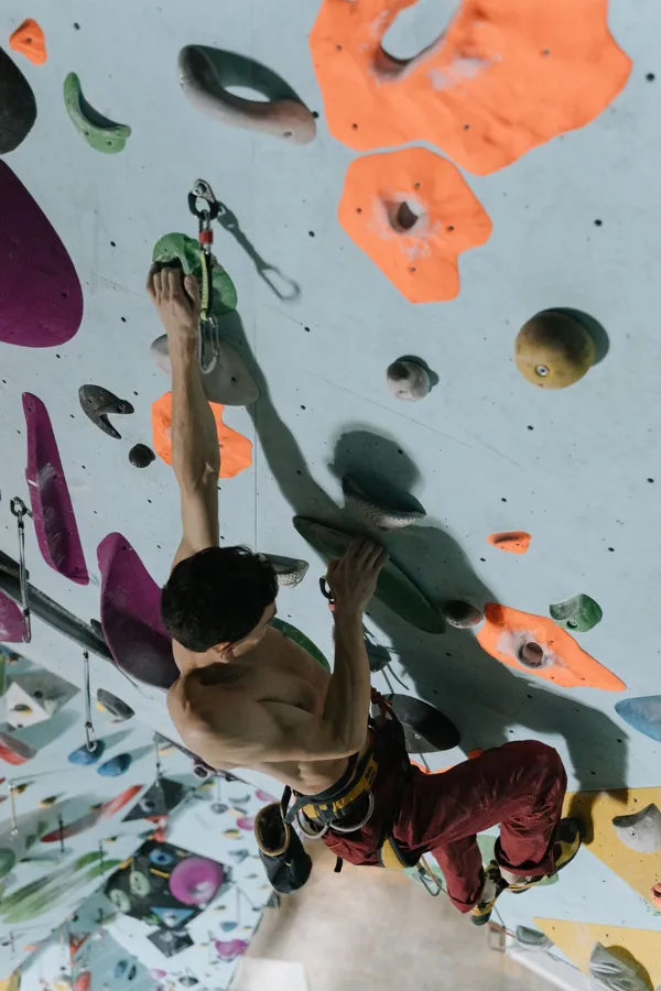 Athletic man practicing climbing on a bright indoor rock wall.