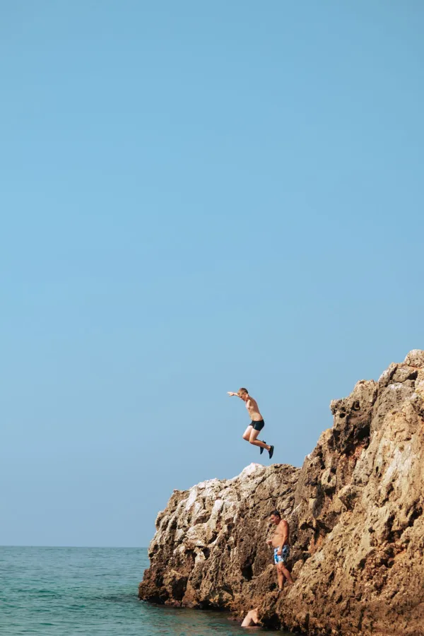 Man jumps from rocky cliff into the ocean at Vlorë County, Albania, a thrilling summer adventure.