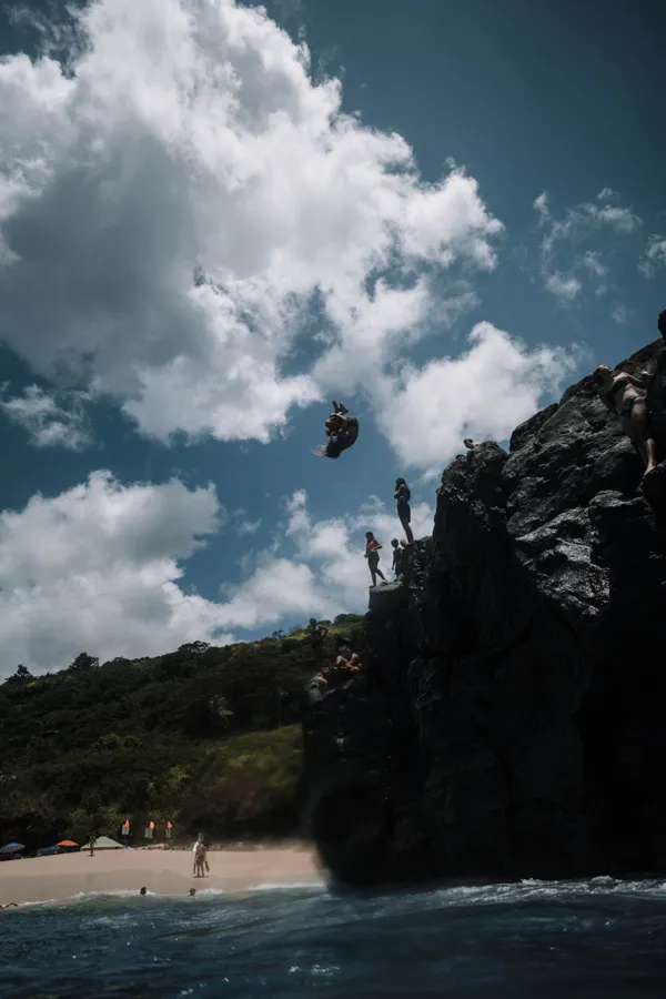 Thrill-seekers enjoy a daring cliff dive into the tropical ocean on a bright summer day.