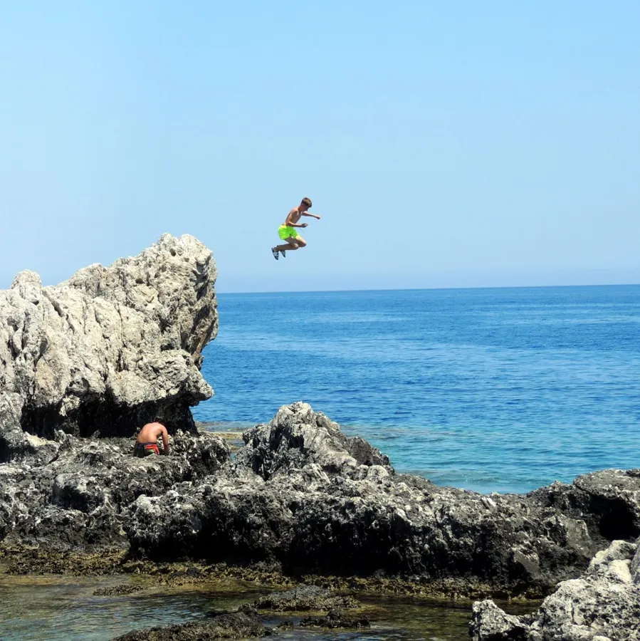 A man leaps from rocky cliffs into the clear blue sea near Lindos, Greece.