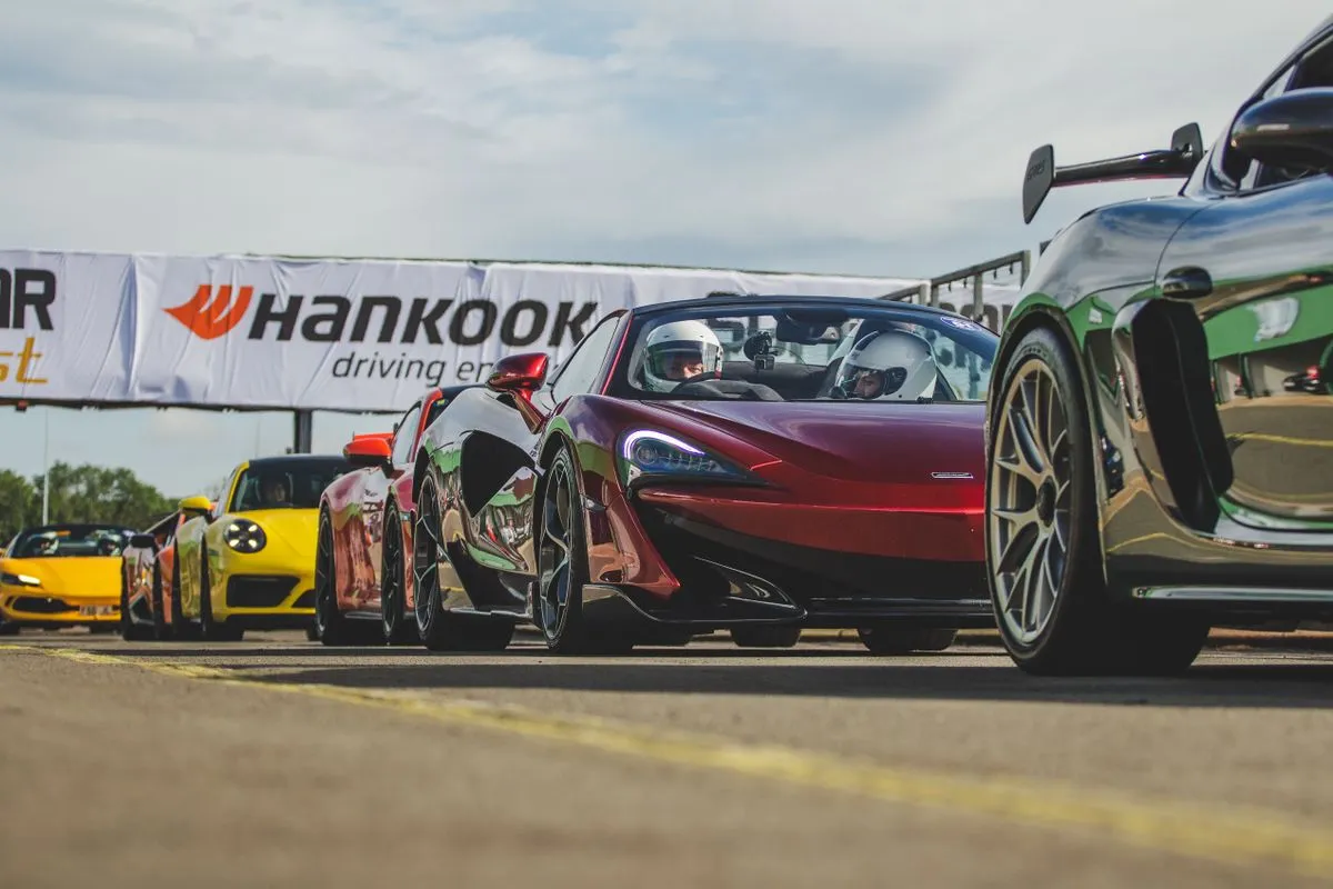 A line of high performance sports cars ready for a driving event at a circuit.