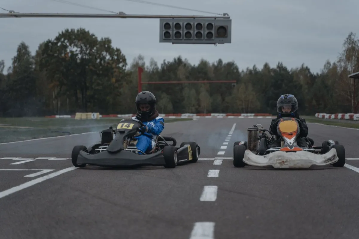 Two go-karts competing fiercely on an outdoor racing track surrounded by trees.
