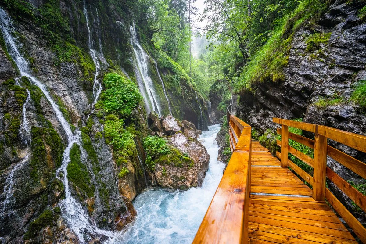 A waterfall in a green gorge with a wooden walkway