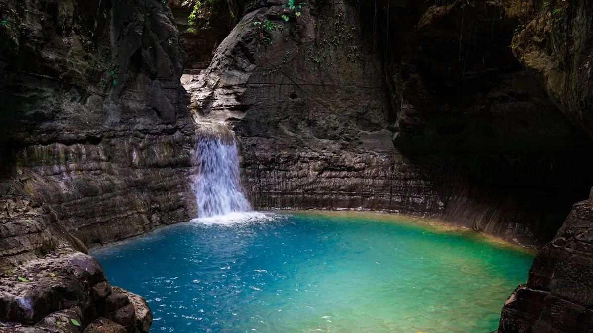 A waterfall flowing into a clear blue pool in a gorge