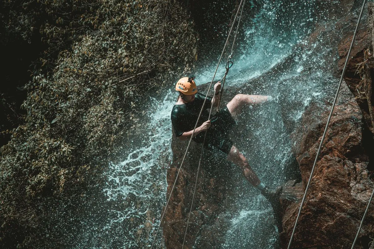A person abseiling down a rock face beside a waterfall in a green gorge