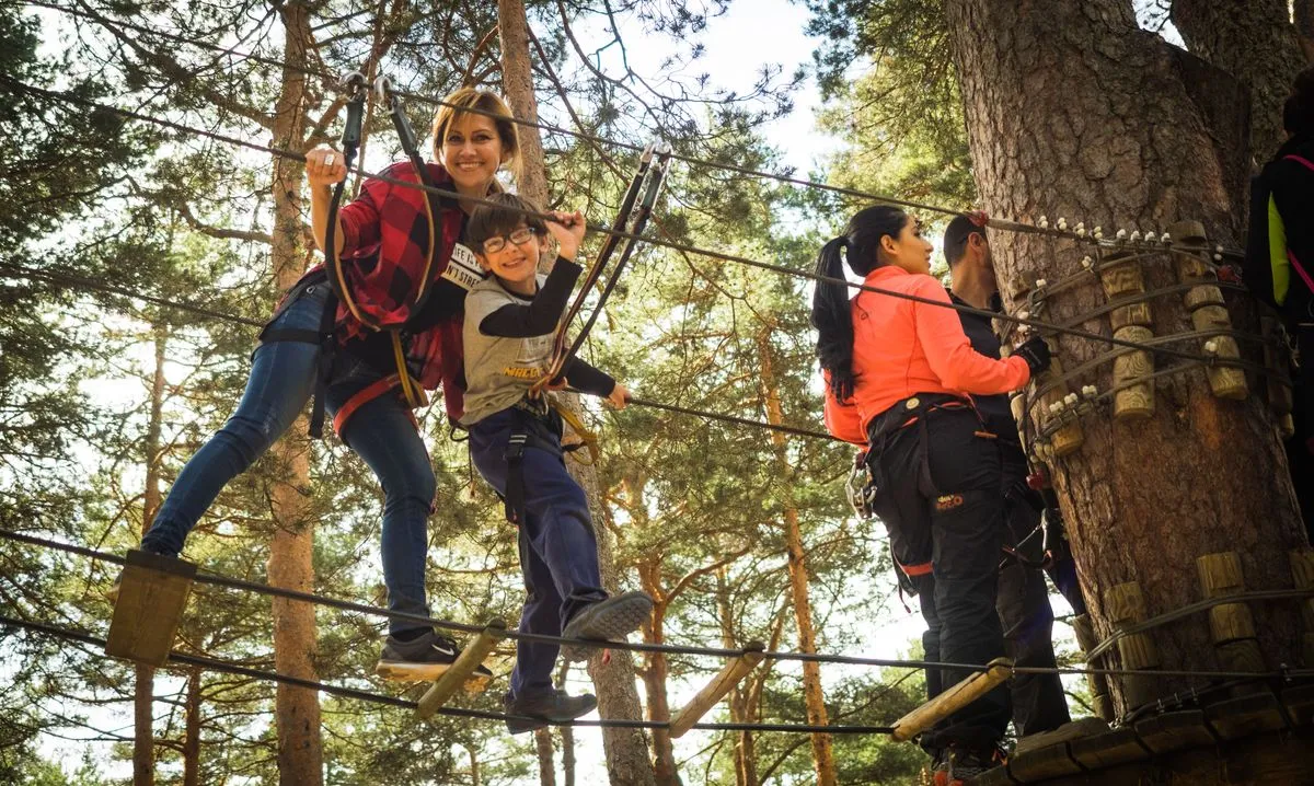Two people crossing a rope bridge between trees on a high ropes course