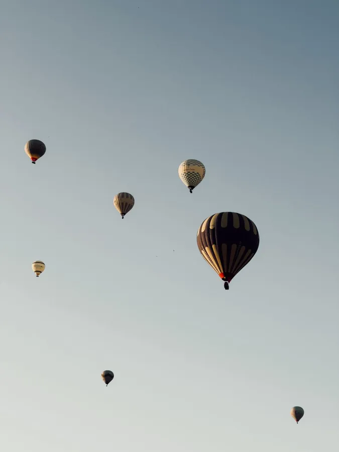 Scenic view of colorful hot air balloons floating in Cappadocia's clear morning sky.