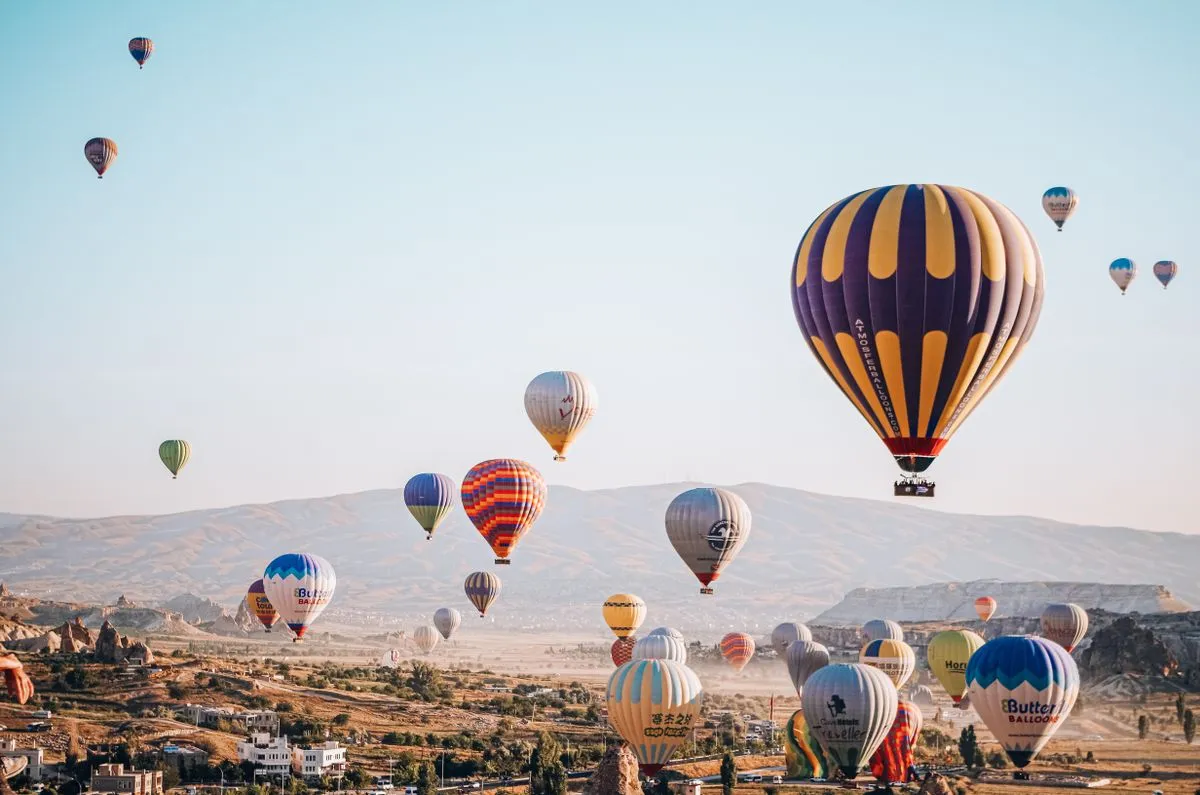 A striped hot air balloon rising above a field with other balloons behind