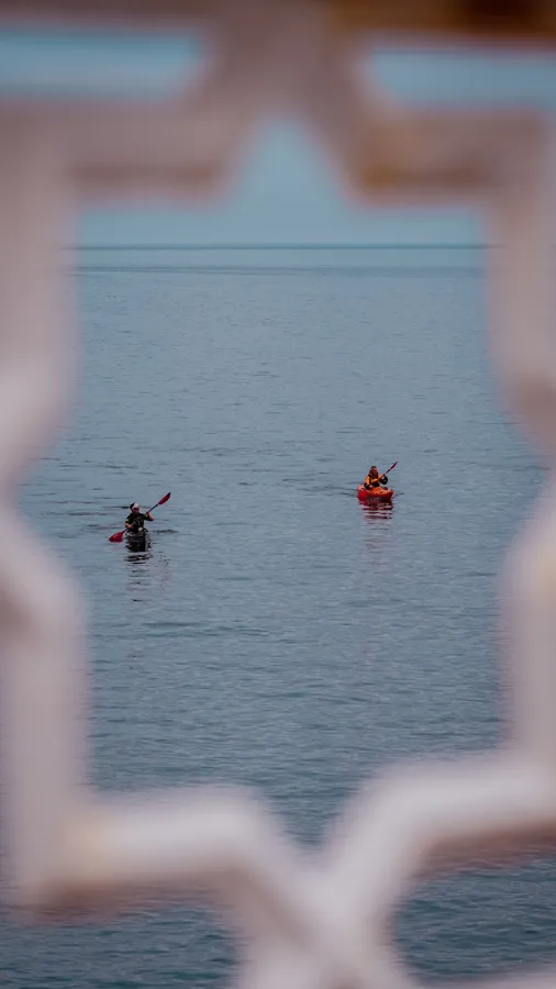 Two kayakers paddle across the serene waters of Llandudno, framed by an ornate structure.