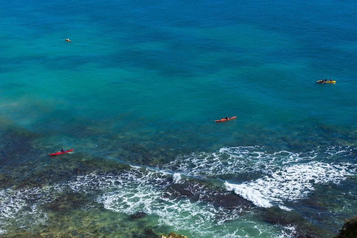 A wide aerial view of people kayaking above clear ocean waters near the Portuguese coast.