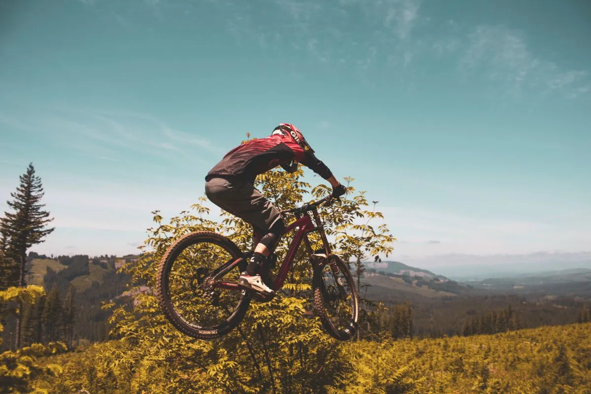A mountain biker in mid air above golden grass with hills behind