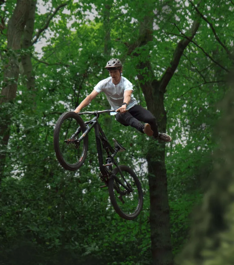 A mountain biker jumping through green woodland