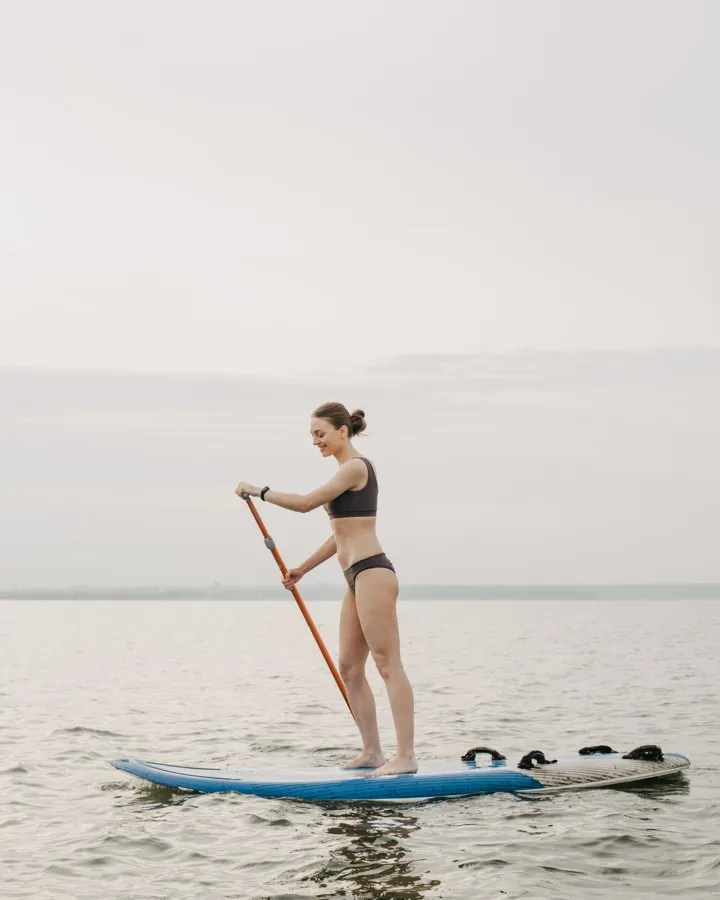 A woman in swimwear paddle boarding on a serene lake during daytime.