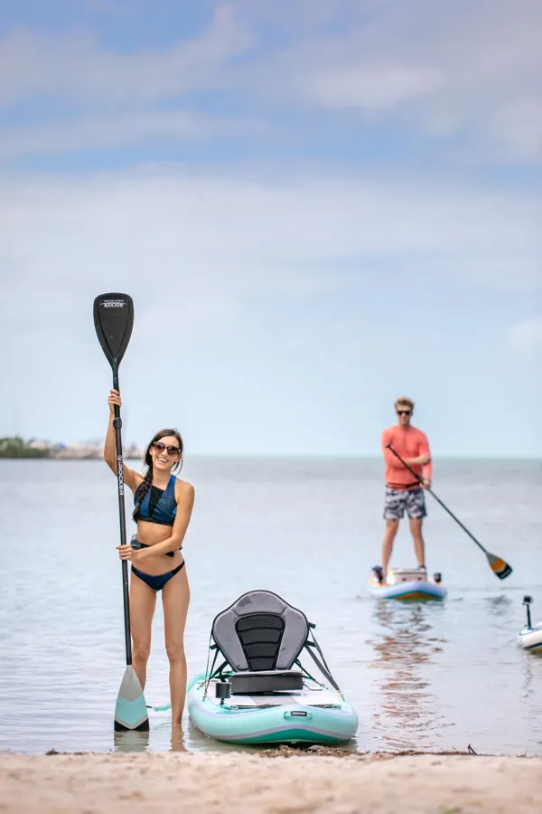 A man and woman paddle boarding on a sunny beach day.