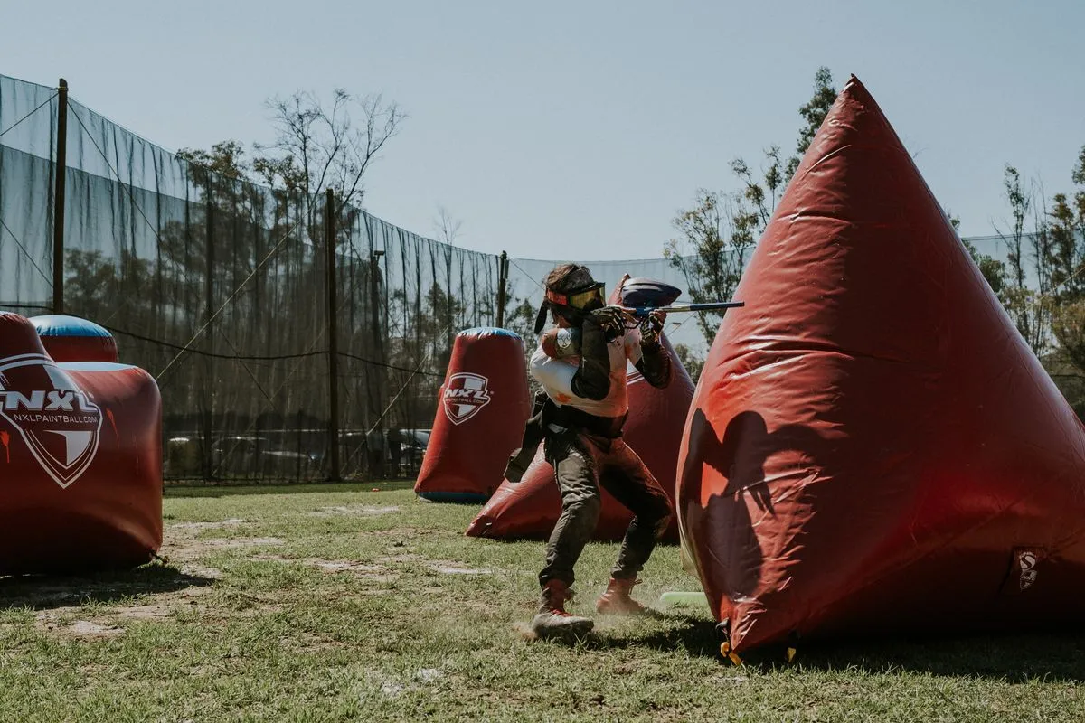 A person actively playing paintball outdoors, aiming behind inflatable covers.