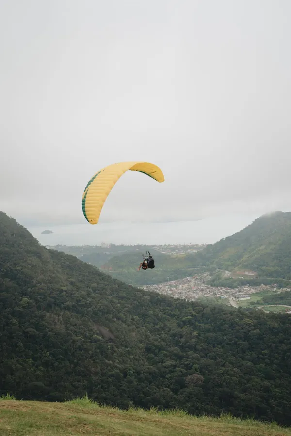 Adventurer enjoys paragliding over a scenic valley on a cloudy day.