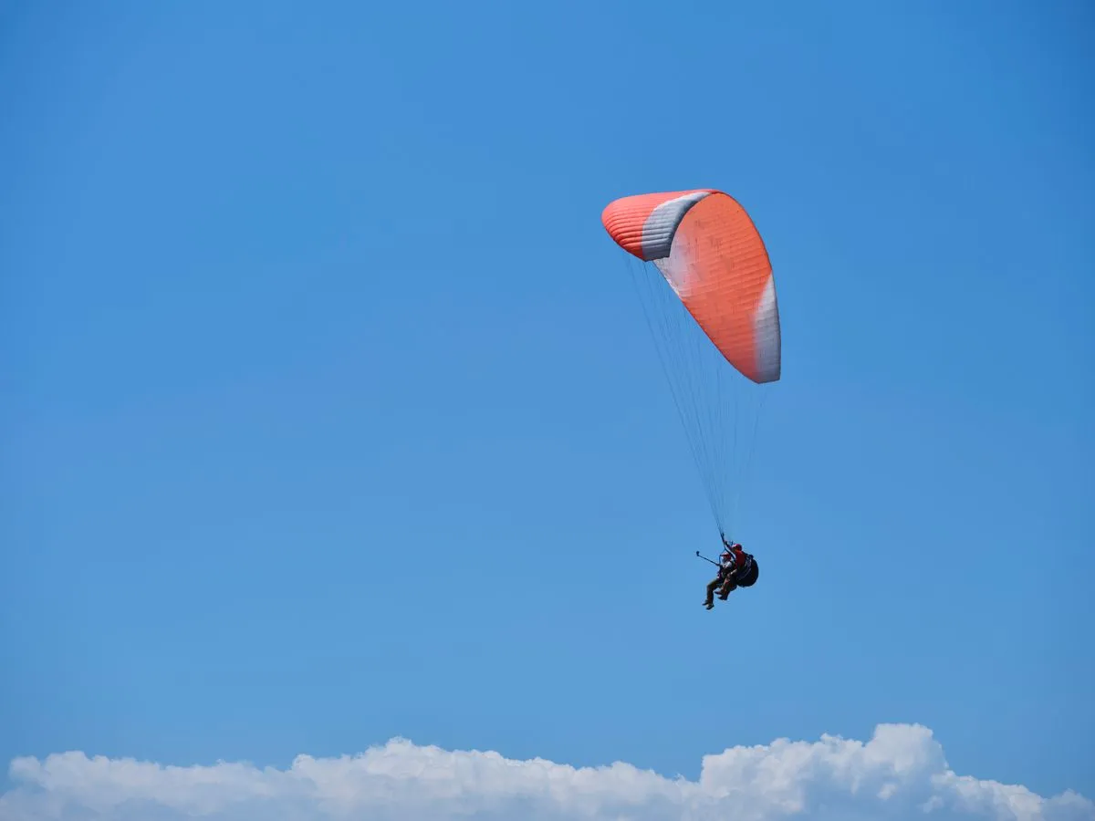 Paraglider soaring gracefully with a bright red parachute against a blue sky backdrop.
