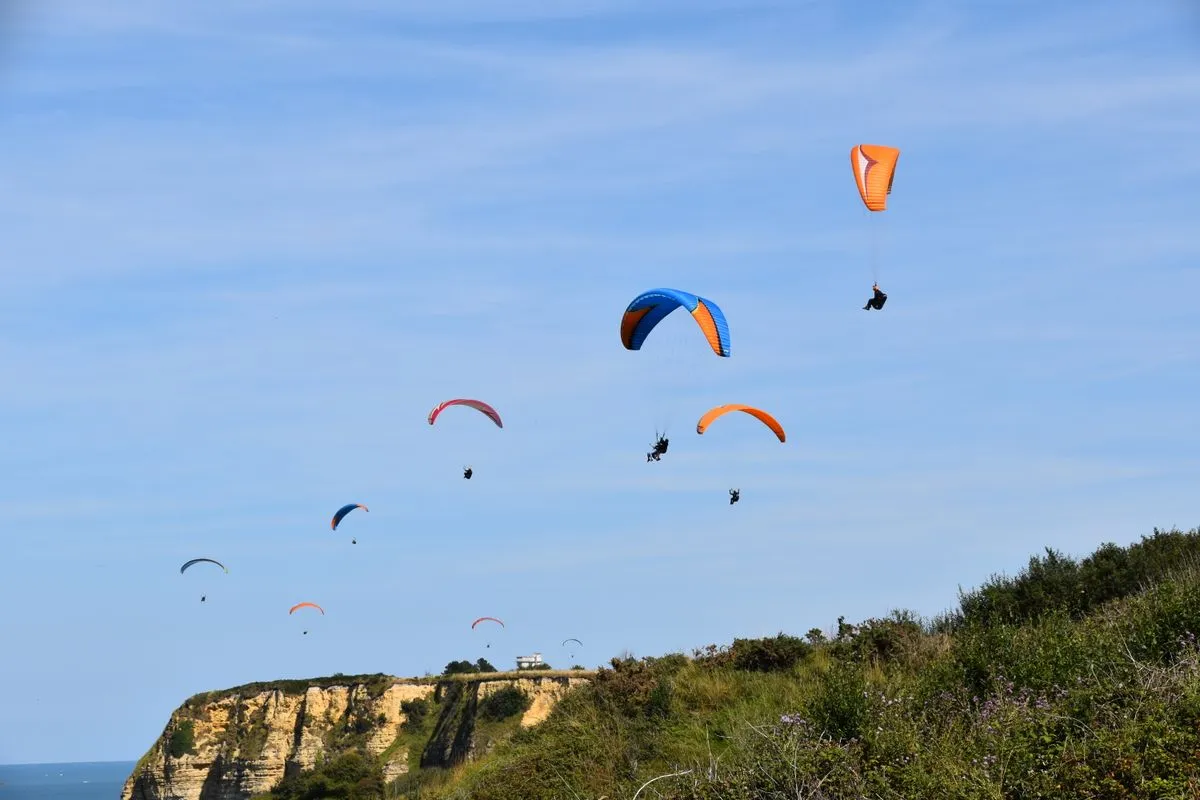 A group of paragliders soar over scenic cliffs on a clear day.