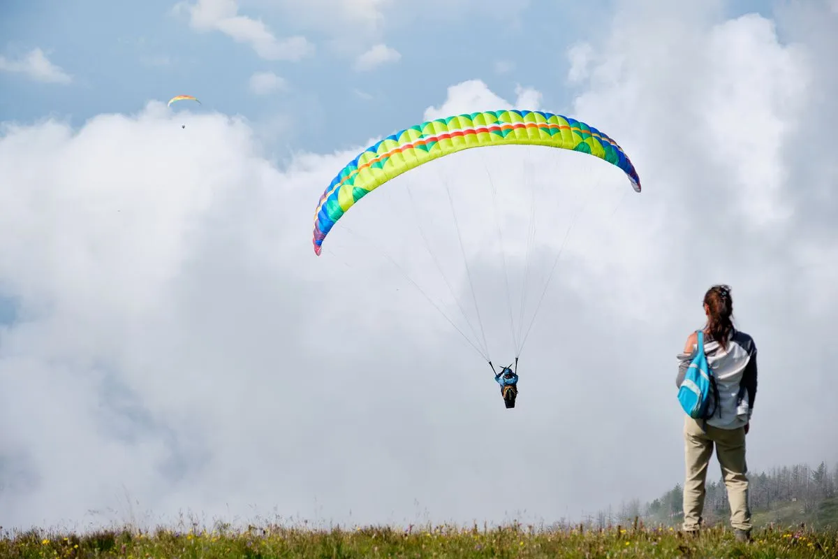 A paraglider with a colourful canopy against a cloudy sky.