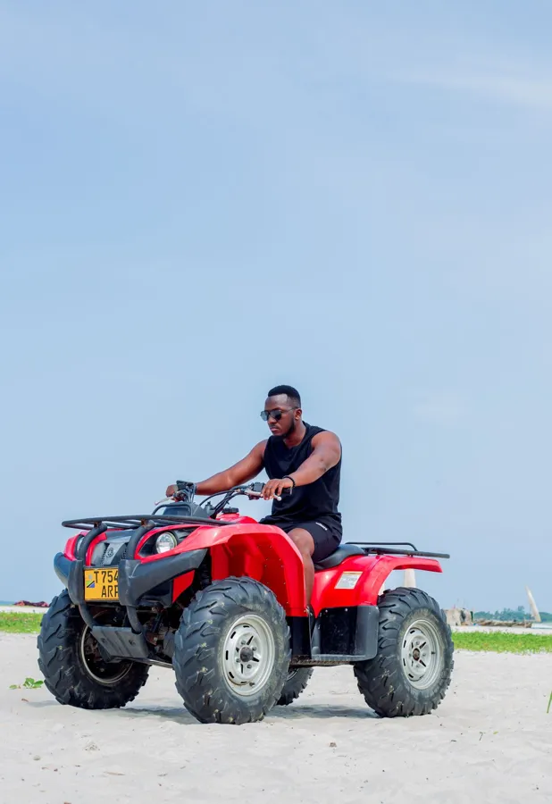 A rider on a red quad bike beside a beach