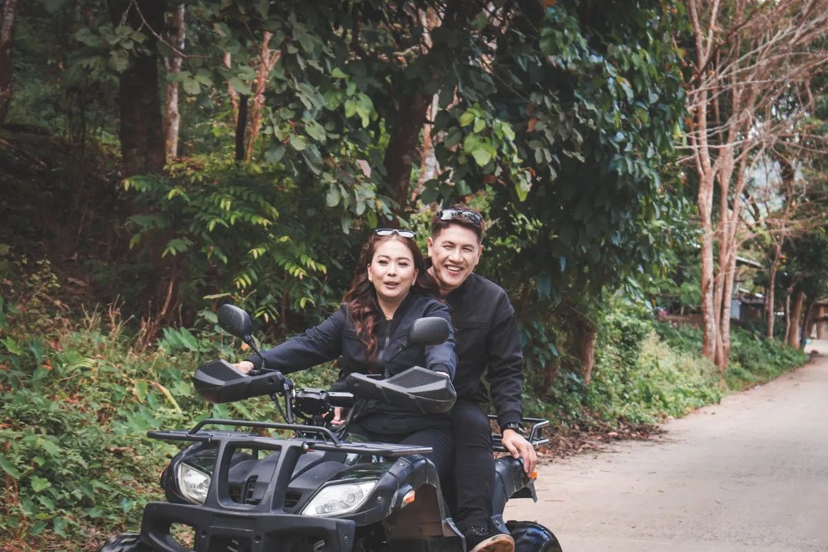 Two people on a quad bike on a tree lined road