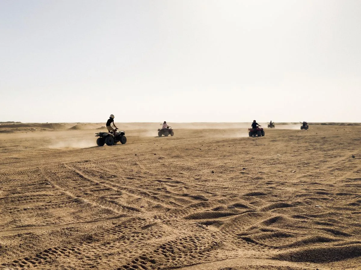 A line of quad bikes kicking up dust across open ground