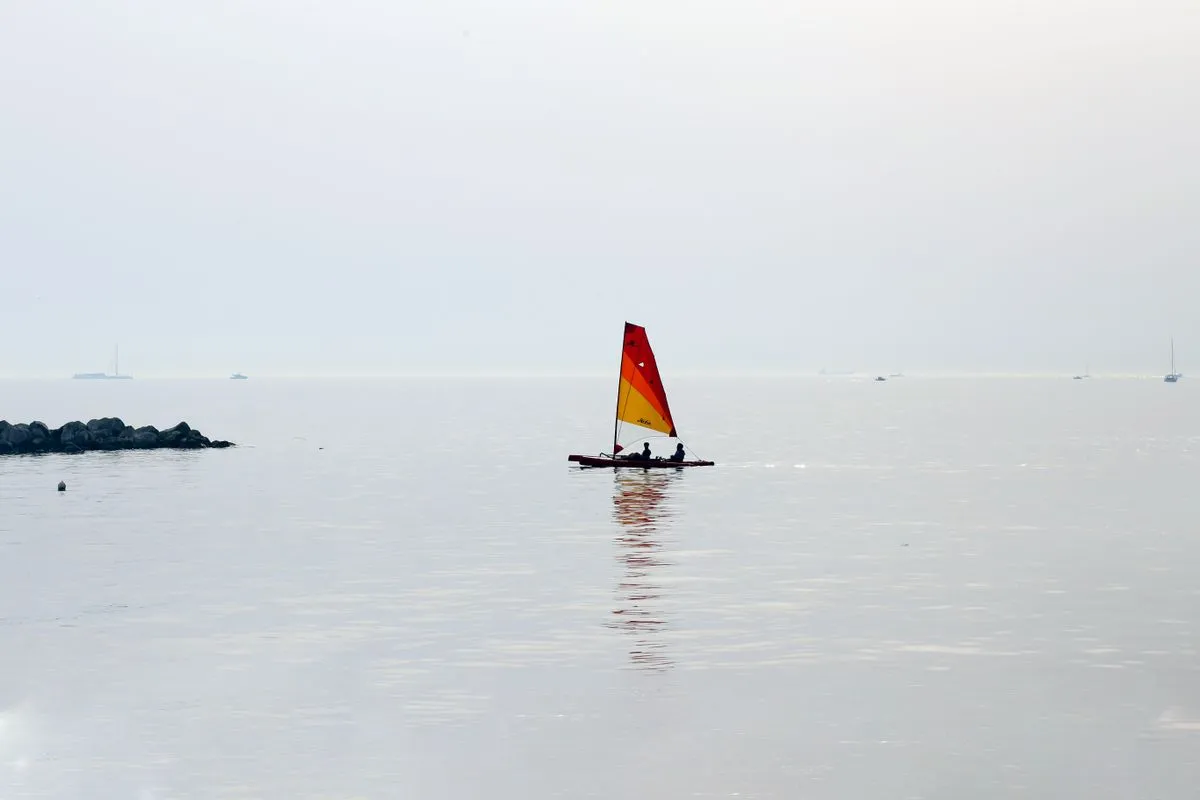A sailboat with bright sails glides peacefully on a calm sea under a clear sky.