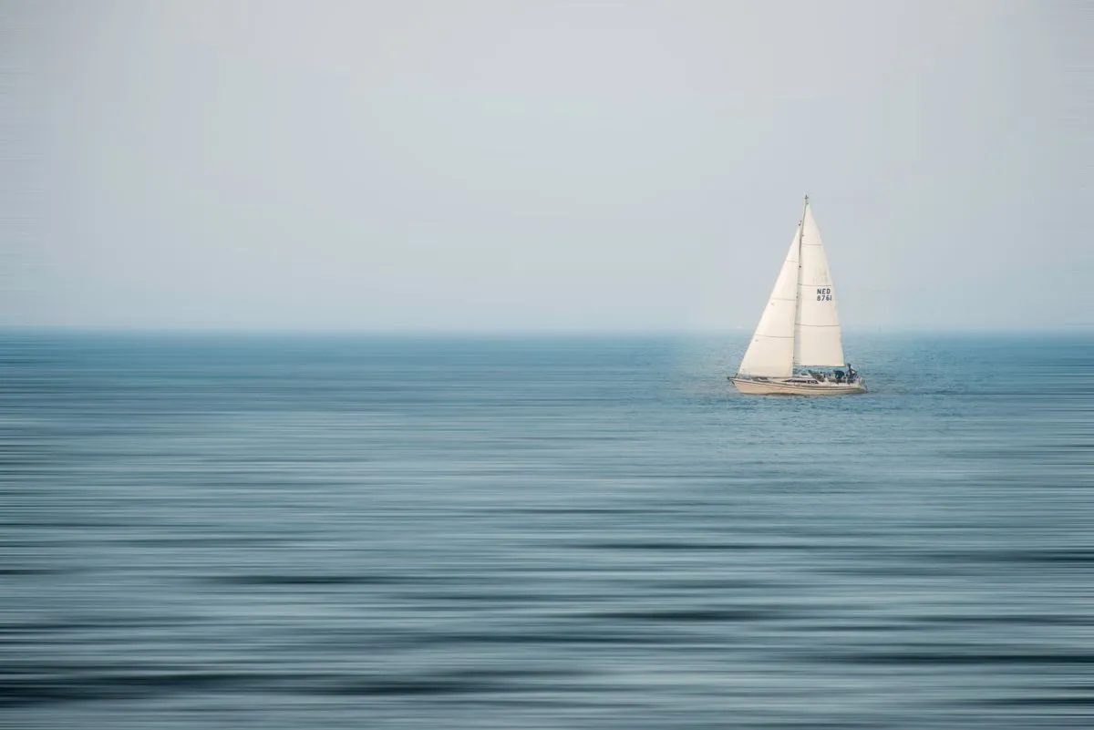 A sailboat glides across a tranquil blue sea.