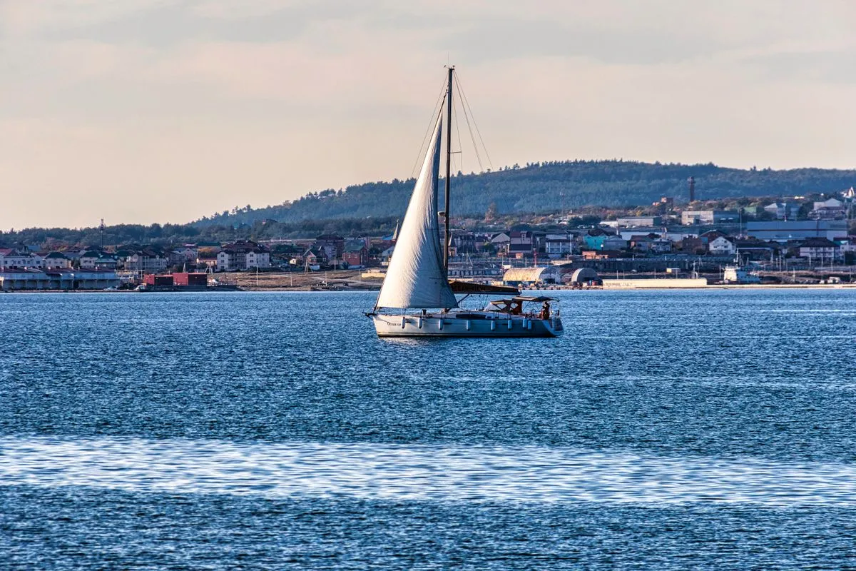 A white sailing boat on blue water near a coastline