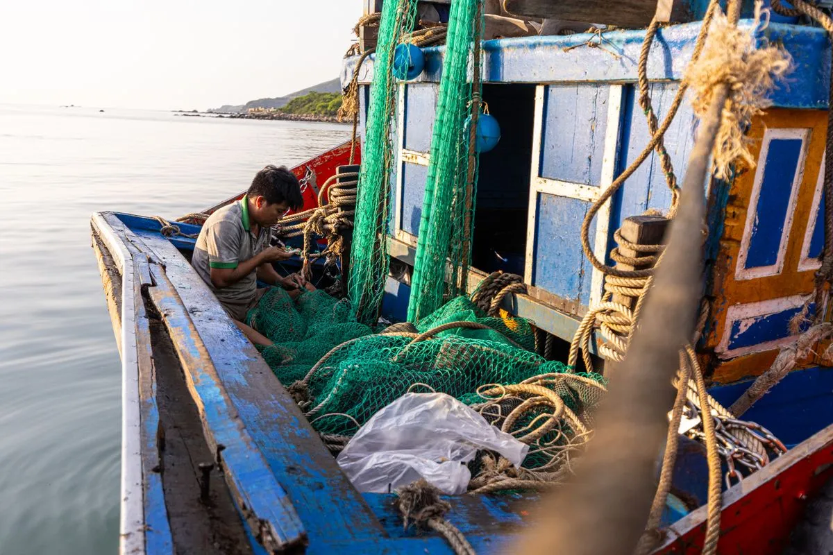 A fisherman repairing nets on a colourful wooden boat