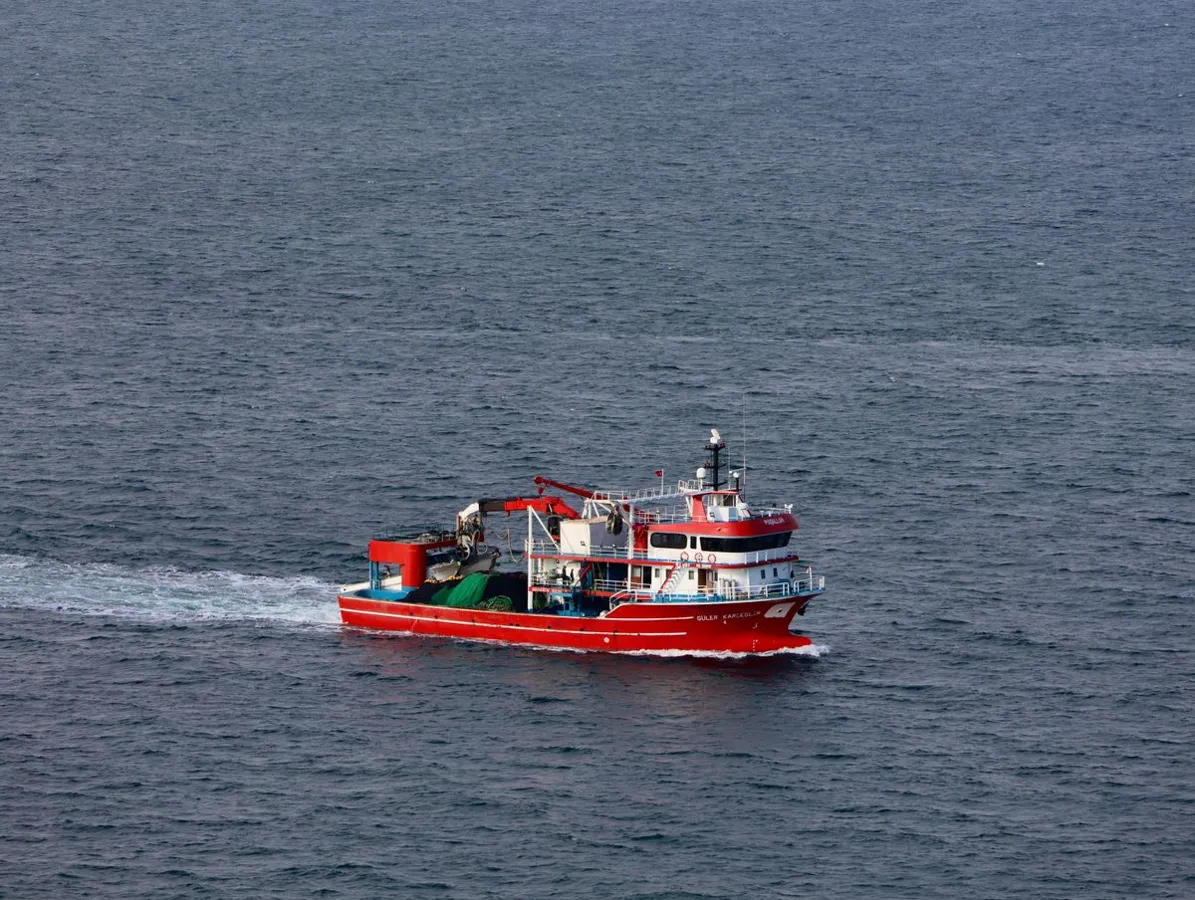A red fishing boat cruising on blue sea water.