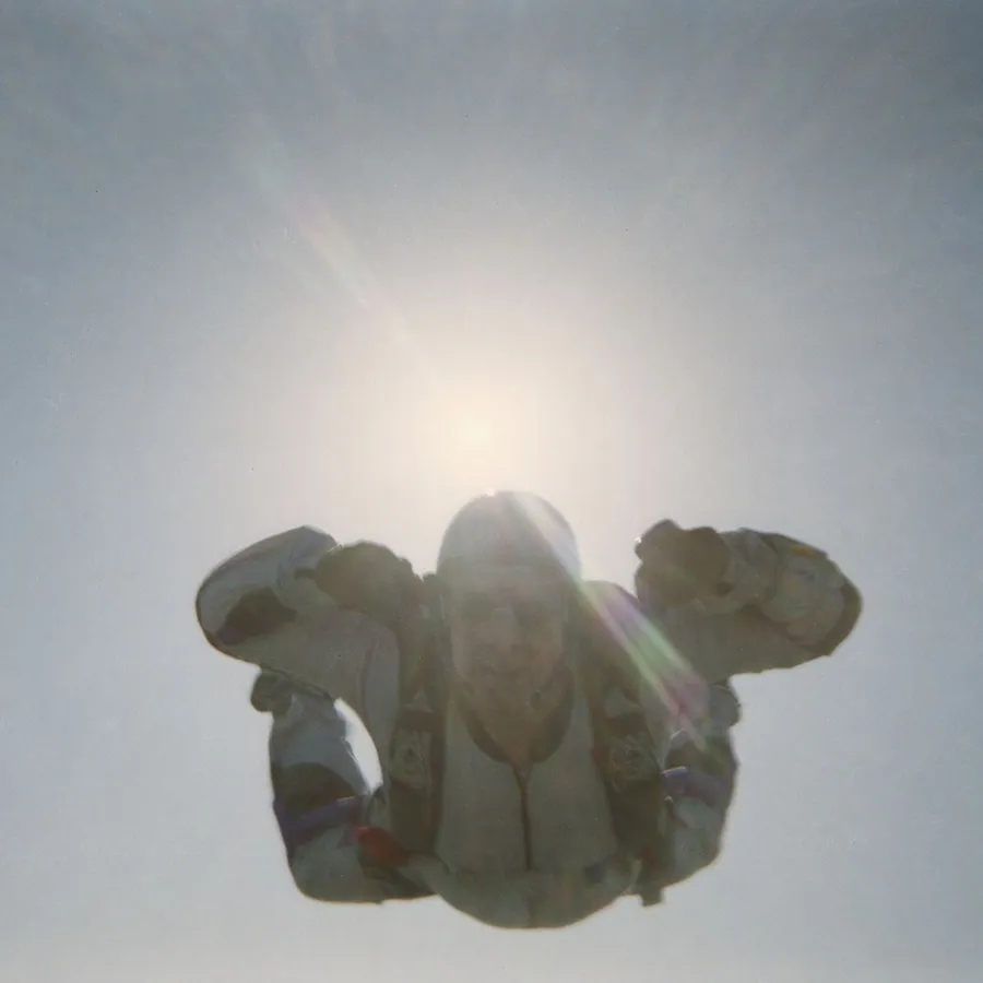 Skydiver in freefall with sun and clear blue sky.