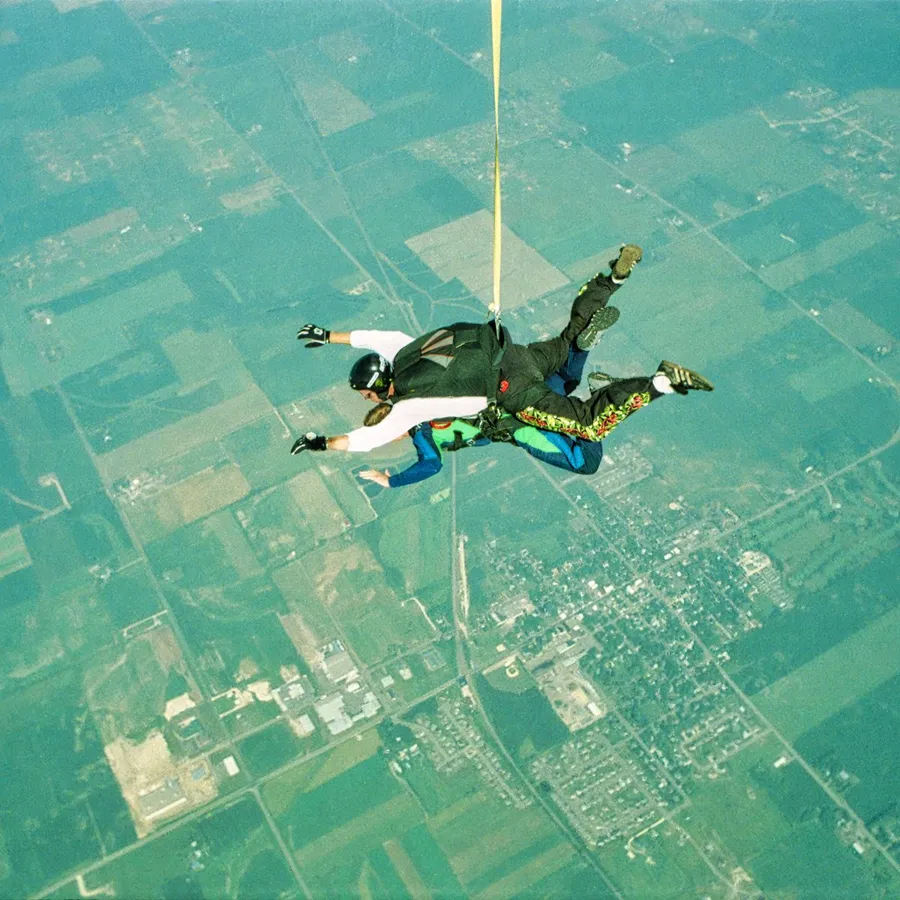 Two skydivers in tandem over a town on a sunny day